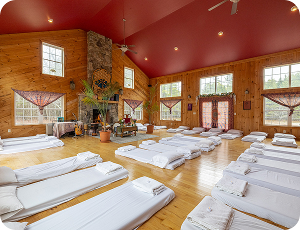The room is set up for plant medicine ceremonies, featuring individual mattresses, pillows, and blankets for participants